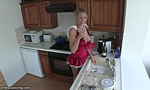 Плавокоса девојка у црвеном подигнутом стану пере судове и изгледа вруће