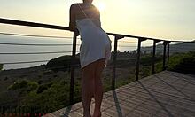 Beyaz saten bir önlük giyen dolgun göğüslü olgun bir kadın, gün batımında balkonda açık havada cinsel aktiviteye giriyor